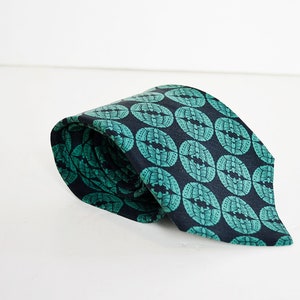 May include: A dark blue tie with a repeating pattern of green circles. The circles have a stylized design inside.
