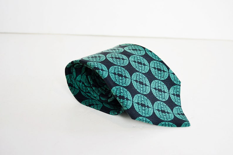 May include: A dark blue tie with a repeating pattern of green circles. The circles have a stylized design inside.