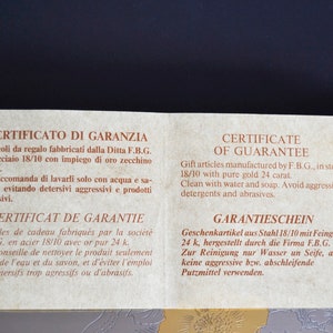 May include: A warranty certificate for gift articles made of steel with 24 karat gold. The certificate is printed in Italian, French, English, and German. It recommends cleaning with water and soap and avoiding aggressive detergents and abrasives.