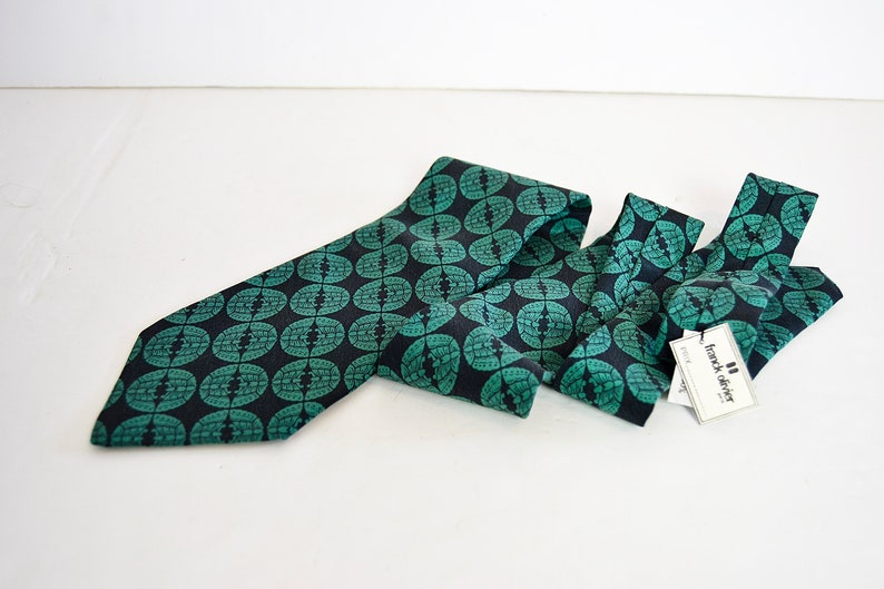 May include: A dark blue tie with a green geometric pattern. The tie has a tag that reads "frank oliver".
