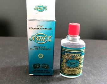 Puede incluir: Una pequeña botella de Eau de Cologne con tapón rojo y caja a juego. La caja y la botella presentan la marca "4711" en una fuente decorativa, con detalles turquesa y dorados. La caja dice "Echt Kölnisch Wasser" y "Original Eau de Cologne."