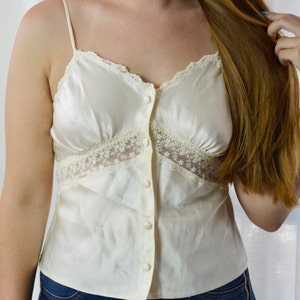 May include: A white satin camisole with lace trim and button closures. The camisole has a relaxed fit and is perfect for layering.