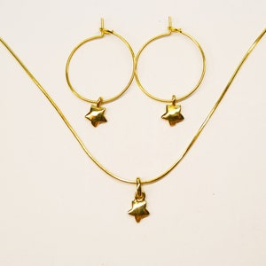 Può includere: Un set di collana e orecchini in oro con ciondoli a forma di stella. La collana è una catena sottile con un piccolo ciondolo a forma di stella. Gli orecchini sono a cerchio con ciondoli a forma di stella.