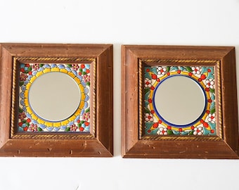 May include: Two square framed mirrors with colourful floral tile designs. The mirrors have a wooden frame with a gold trim.