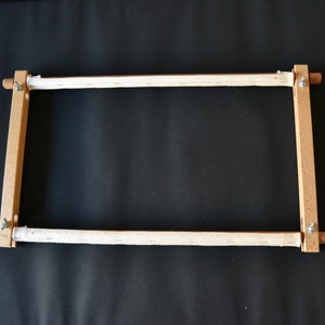 Puede incluir: Un aro de bordado de madera con una tela blanca estirada sobre él. El aro se utiliza para el bordado a mano y es ajustable para adaptarse a diferentes tamaños de tela.