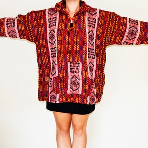 May include: A red, orange, pink, and blue patterned sweater with a zipper closure. The sweater has a geometric design.