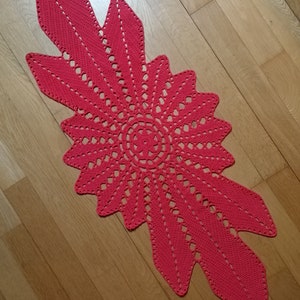 Peut inclure: Un chemin de table en crochet rouge avec un motif de feuille. Le chemin de table a un grand motif circulaire en crochet au centre.