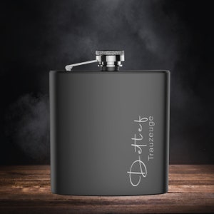 Könnte beinhalten: Eine schwarze Metallflasche mit einem silbernen Verschluss und einer weißen Aufschrift "Deft - Trauzeuge".