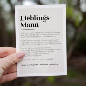 May include: A white card with black text that reads "Lieblings-Mann" and a description of a person who is a partner, best friend, and source of happiness. The text also includes the synonyms "Seelenpartner", "Traummann", and "Herzensk&ouml;nig".
