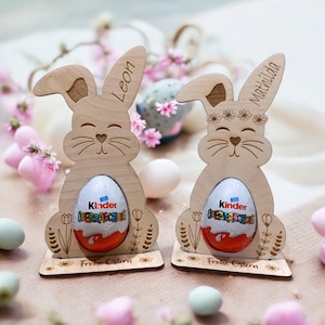 Könnte beinhalten: Zwei hölzerne Osterhasen-Eierhalter mit den Namen Leon und Matilda eingraviert. Jeder Halter hat ein Schokoladenei drin und die Worte "Frohe Ostern" unten.