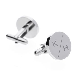 May include: A pair of silver cufflinks with a round, engraved design. The cufflinks feature the initials "K/H" in a simple, modern font.