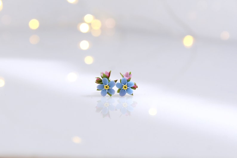 May include: A pair of blue forget-me-not flower earrings with pink buds and green leaves.