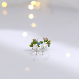 May include: A pair of silver stud earrings with small blue and pink flower accents. The flowers have green leaves.