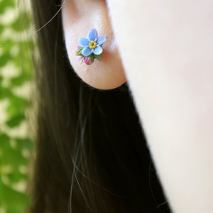 May include: A pair of small blue forget-me-not flower earrings with yellow centers and pink accents.