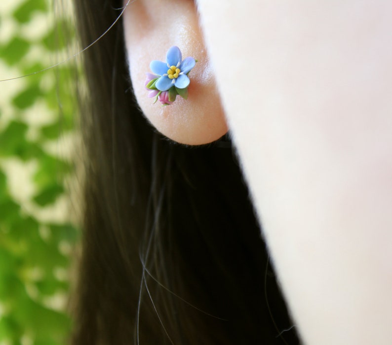 May include: A pair of small blue forget-me-not flower earrings with yellow centers and pink accents.