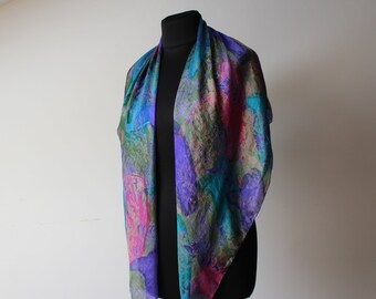 May include: A colorful silk scarf with a vibrant floral pattern. The scarf features shades of blue, purple, pink, and green. The scarf is draped over a black mannequin, showcasing its flowing design and intricate details.