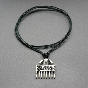 Puede incluir: Un collar con un colgante de plata con un dise&ntilde;o de nudo celta y una parte inferior en forma de peine. El collar est&aacute; en un cord&oacute;n negro.