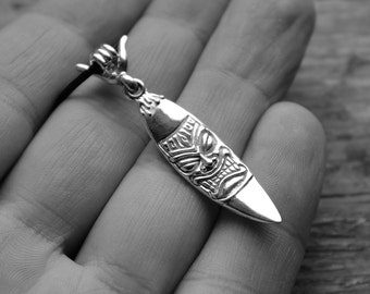 May include: Silver surfboard necklace with a tiki face carving. The necklace is on a black cord and has a silver hand charm.