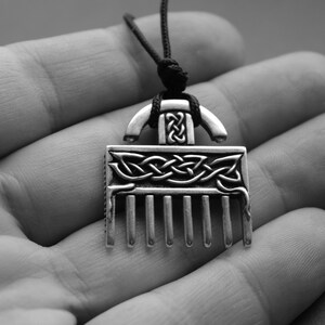 Puede incluir: Un collar con un colgante de plata en forma de peine y con un dise&ntilde;o de nudo celta. El colgante est&aacute; colgado de un cord&oacute;n negro.
