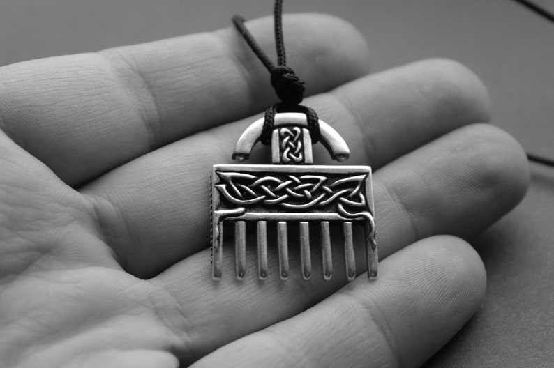 Puede incluir: Un collar con un colgante de plata en forma de peine y con un dise&ntilde;o de nudo celta. El colgante est&aacute; colgado de un cord&oacute;n negro.