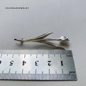 May include: A silver tulip brooch, approximately 5 cm in length. The brooch features detailed leaves and a delicate flower head. The jewelry is set against a neutral background. The text "VOLODARJEWELRY" is visible in the upper left corner.