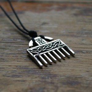 Puede incluir: Un collar con un colgante de plata en forma de peine y con un dise&ntilde;o de nudo celta. El colgante est&aacute; en un cord&oacute;n negro.