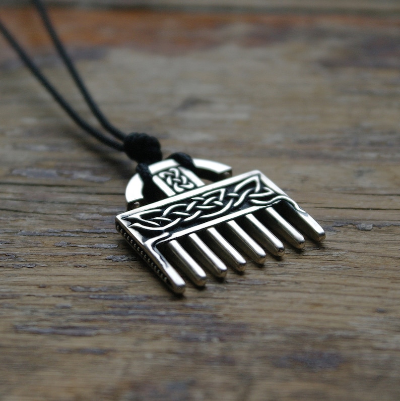 Puede incluir: Un collar con un colgante de plata en forma de peine y con un dise&ntilde;o de nudo celta. El colgante est&aacute; en un cord&oacute;n negro.