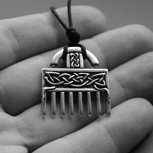Puede incluir: Un collar con un colgante de plata en forma de peine y con un dise&ntilde;o de nudo celta. El colgante est&aacute; colgado de un cord&oacute;n negro.