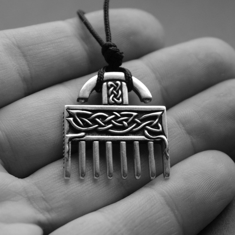 Puede incluir: Un collar con un colgante de plata en forma de peine y con un dise&ntilde;o de nudo celta. El colgante est&aacute; colgado de un cord&oacute;n negro.