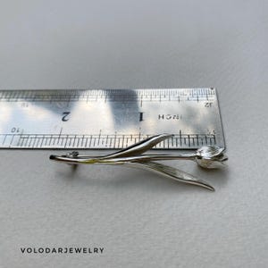 May include: A silver tulip brooch with detailed leaves and petals. The brooch is approximately 5 cm long, as measured by a ruler. The brooch is a floral accessory, perfect for adding a touch of nature-inspired elegance to any outfit.