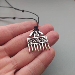 Puede incluir: Un collar con un colgante de plata en forma de peine y con un dise&ntilde;o de nudo celta. El colgante est&aacute; en un cord&oacute;n negro.