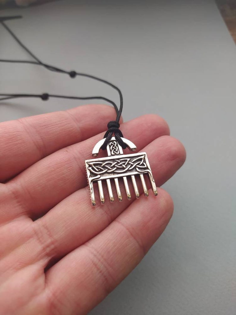 Puede incluir: Un collar con un colgante de plata en forma de peine y con un dise&ntilde;o de nudo celta. El colgante est&aacute; en un cord&oacute;n negro.