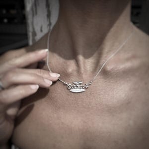 Könnte beinhalten: Eine silberne Halskette mit einem Surfbrett- und einem Wal-Anhänger. Der Anhänger trägt die Aufschrift "Ocean Born".
