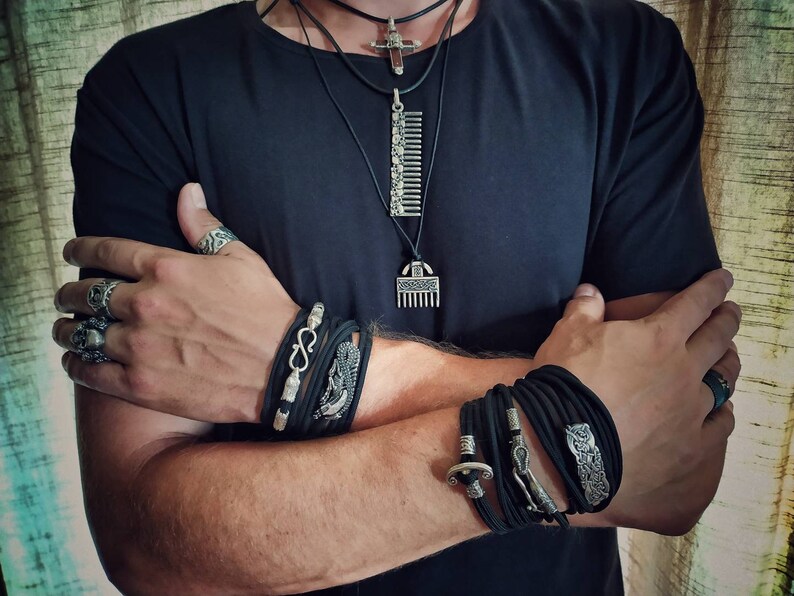 Puede incluir: Una persona lleva una camiseta negra con m&uacute;ltiples pulseras y anillos de plata. Las pulseras son de cuero negro y tienen detalles plateados. Los anillos tambi&eacute;n son de plata y tienen varios dise&ntilde;os.