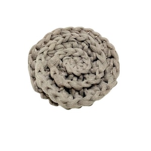 May include: A handmade, gray crocheted coaster with a spiral design. The coaster is round and made of thick, textured yarn. The neutral color and simple design make it a versatile addition to any home decor.
