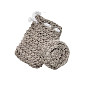 May include: A handmade, gray knitted basket with a matching round coaster. The basket has a rectangular shape with a white trim and a looped handle. The coaster is a tightly coiled circle. The items are made of a thick, textured yarn.