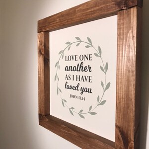 Love One Another Wall decor with wooden stained frame. Bible verse sign white background with Mossy green color wreath.