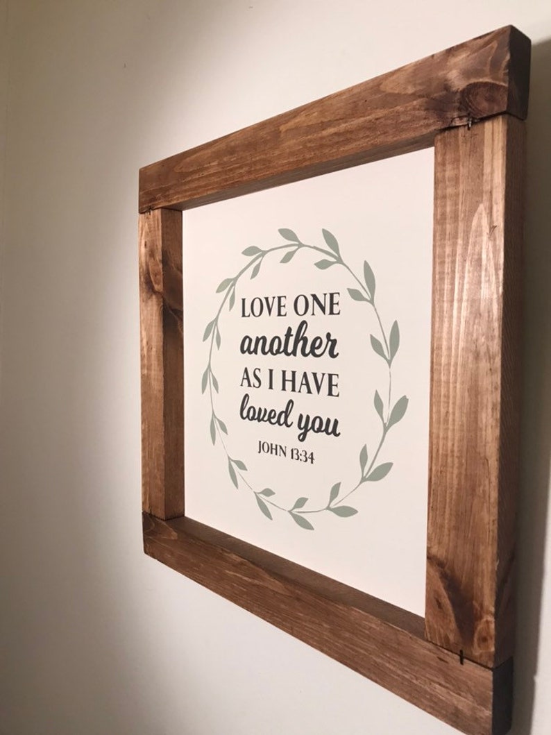 Love One Another Wall decor with wooden stained frame. Bible verse sign white background with Mossy green color wreath.