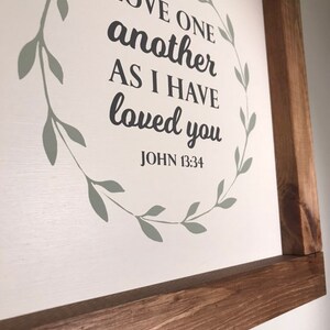 Love One Another Wall decor with wooden stained frame. Bible verse sign white background with Mossy green color wreath.