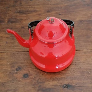 Peut inclure: Une théière en émail rouge vif avec une poignée et un couvercle noirs. La théière a un corps arrondi et un bec.