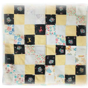May include: A patchwork quilt with a square pattern. The quilt features squares of various colors and patterns, including floral prints, solid yellow, black with teapot designs, and white. The quilt is bordered with a light blue fabric.
