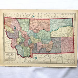 May include: Vintage map of Montana, featuring a detailed depiction of the state's counties in various pastel colors. The map includes the text "Montana" and "The Geographical Pub. Co., Chicago". The map is framed by a red border and is printed on aged paper.