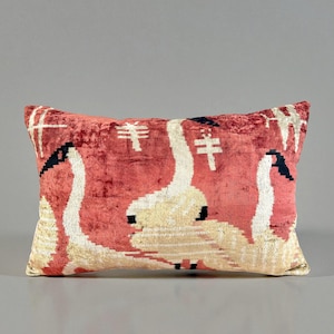 May include: A rectangular cushion featuring a red background with a pattern of white swans. The swans have black beaks and are arranged in a repeating design. The cushion has a soft, textured appearance.