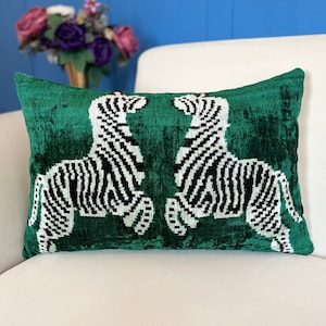 May include: A green velvet cushion with a white and black zebra print design. The zebras are facing each other.