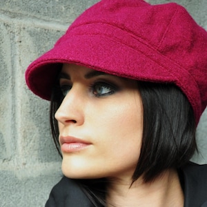 Peut inclure: Une femme portant une casquette de newsboy en laine rouge foncé avec une coupe au carré courte. La casquette a une visière légèrement incurvée et un tissu doux et texturé.