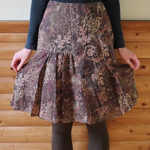 Puede incluir: Una falda floral marrón y crema con un diseño plisado. La falda es de largo hasta la rodilla y tiene una cintura ajustada.
