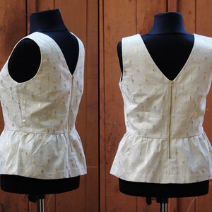 May include: A white sleeveless top with a gold pattern and a zipper down the back. The top has a peplum hemline.