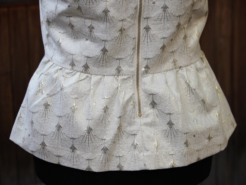 May include: A white top with a gold pattern and a zipper down the back. The top has a ruffled hem.
