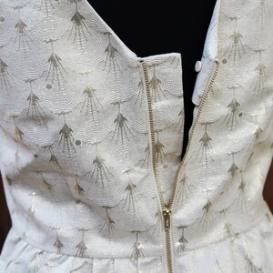 May include: A white dress with a gold pattern and a zipper down the back.