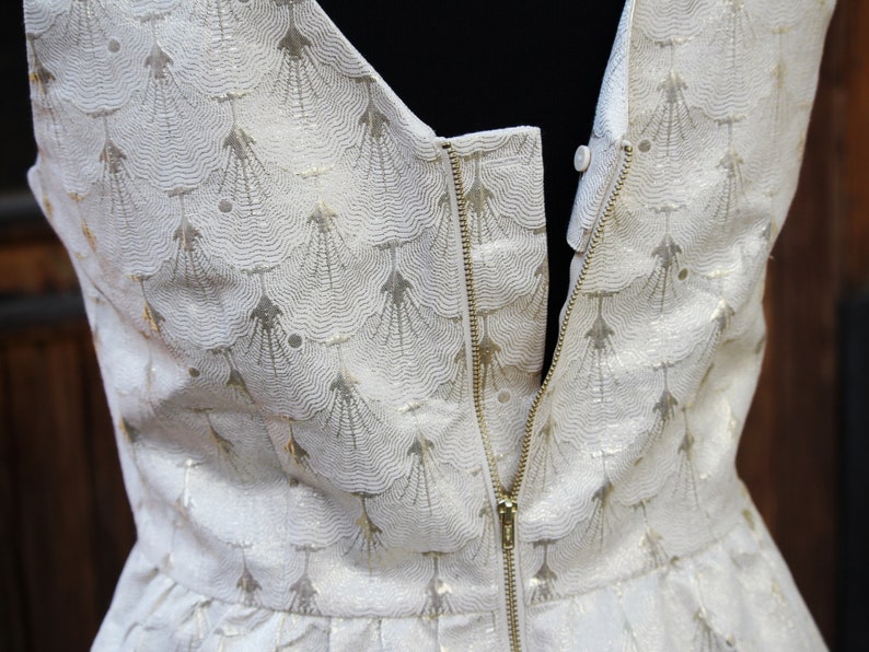 May include: A white dress with a gold pattern and a zipper down the back.